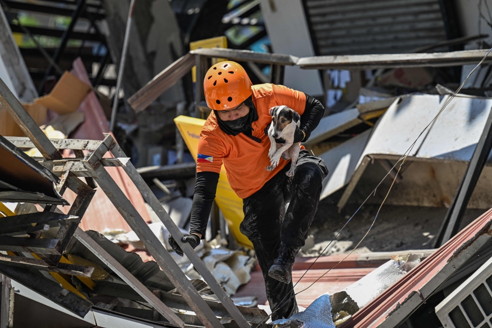 A responder carries a rescue dog while conducting search and rescue operations in a collapsed building after a 7.8 magnitude earthquake in General Santos City on June 9, 2026. — AFP pic 