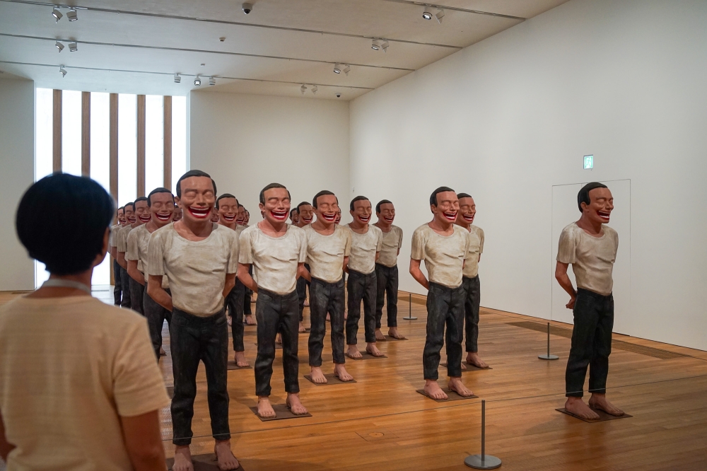 A visitor of the 'M+ Sigg Collection: Inner Worlds' exhibition is seen here looking at artist Yue Minjun’s artwork called '2000 A.D.', where 25 life-sized sculptures are arranged like the famous terracotta warriors in Emperor Qin Shihuang’s mausoleum. — Picture by Ida Lim