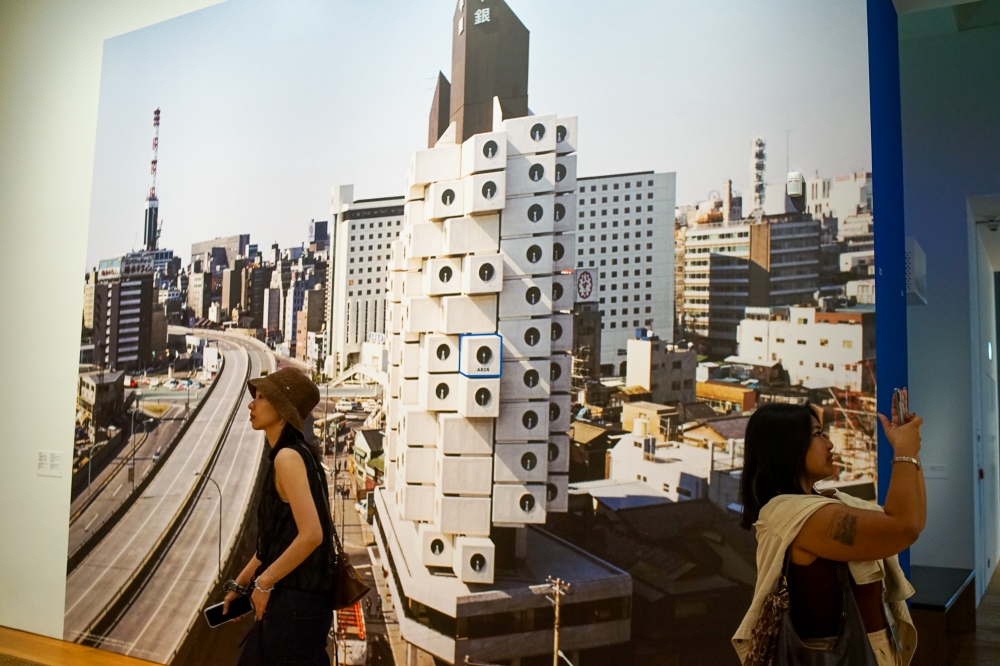 Visitors at M+ walk past a photograph of the Nakagin Capsule Tower, with a box marked with blue outlines being Unit A806’s location in the building which has since been demolished. — Picture by Ida Lim