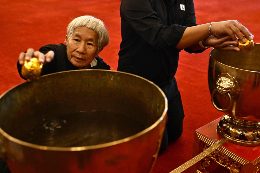 A member of the public dips a cup while paying respects in front of a portrait of the late Thai Princess Bajrakitiyabha Mahidol in the royal throne hall at the Grand Palace in Bangkok on June 13, 2026. — AFP pic