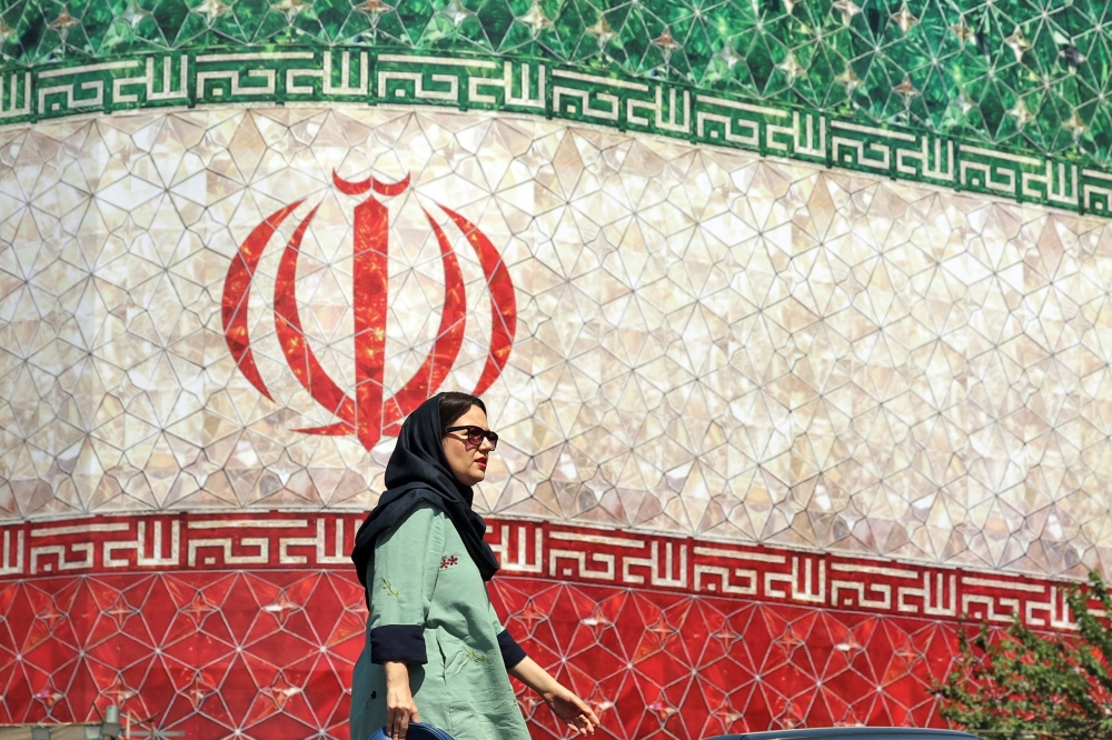 A woman walks past a billboard displaying Iran’s national flag at Enghelab Square in Tehran on June 14, 2026. — AFP pic